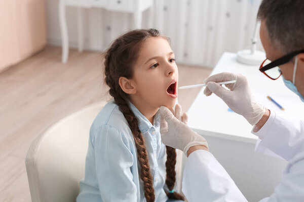 Doctor examining little girl with sore throat in clinic