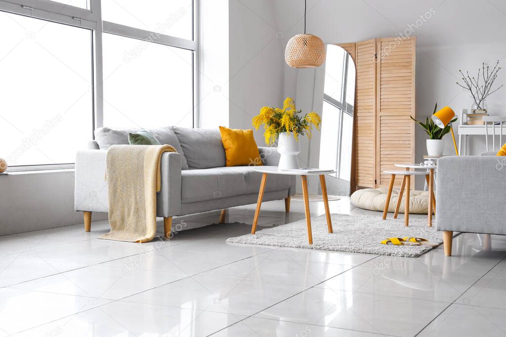 Vase with mimosa flowers on table and sofa in interior of living room