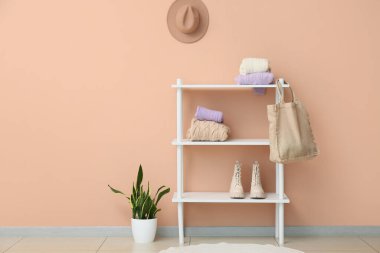 Raflarda örgü süveterler, alışveriş çantası ve bej duvarın yanında ayakkabılar.