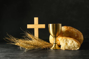 Koyu arkaplanda haç ve ekmek dolu bir bardak şarap.