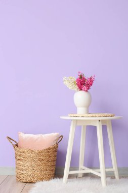 Masada sümbül çiçekli vazo ve odada renk duvarına yakın yastıklı hasır sepet.