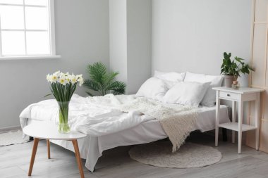 Hafif yatak odasının içinde vazodaki nergisler ve ev bitkileri var.