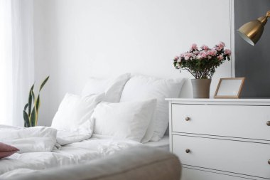 Begonya çiçekleri, boş fotoğraf çerçevesi ve yatak odasındaki ışık duvarının yanındaki çekmecelerin üzerindeki lamba.