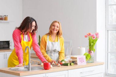 Mutlu genç bir kadın ve annesi evde birlikte yemek pişiriyorlar. Uluslararası Kadınlar Günü kutlamaları