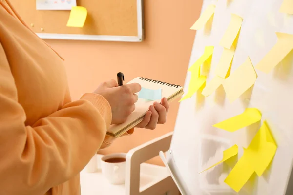 Mujer Escribiendo Cuaderno Cerca Rotafolio Con Notas Adhesivas Habitación —  Fotos de Stock