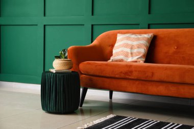 Yeşil duvarın yanında pouf ve kırmızı kanepe sepetli defter.