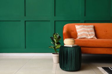 Yeşil duvarın yanında pouf ve kırmızı kanepe sepetli defter.