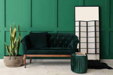 Şık oturma odasının içinde kanepe, ayna ve puf renkli duvarın yanında.