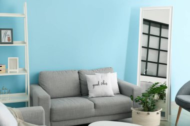 Oturma odasındaki renkli duvarın yanında rahat bir kanepe ve ayna.