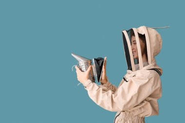 Mavi arka planda sigara içen koruyucu kıyafetli kadın arıcı.