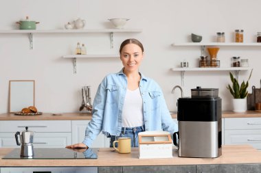 Mutfakta kahve makinesiyle tezgahın yanında gülümseyen genç bir kadın.
