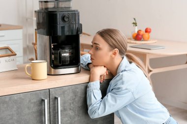 Mutfakta kahve makinesiyle tezgahın yanında genç bir kadın.