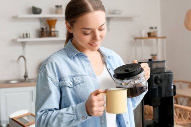 Genç bir kadın mutfakta demlikten sıcak kahve dolduruyor.