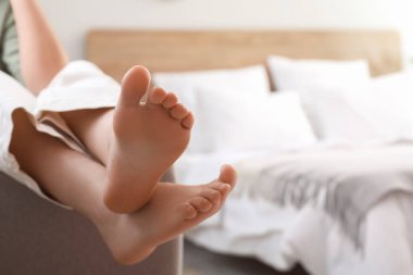 Evdeki koltukta oturan çıplak ayaklı genç kadın, yakın plan.