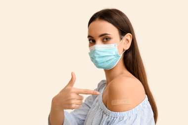 Maskeli genç kadın beyaz arka planda uygulamalı tıbbi yama gösteriyor.