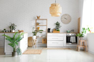 Tezgahları, çiçekleri ve saati olan modern mutfağın içi.