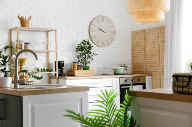 Tezgahları, çiçekleri ve saati olan modern mutfağın içi.