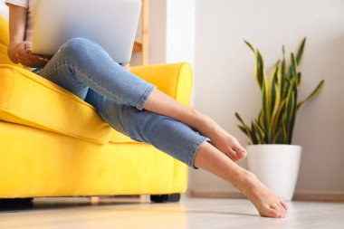 Evdeki kanepede dizüstü bilgisayarlı çıplak ayaklı bir kadın oturuyor.