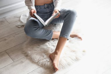 Çıplak ayaklı kadın mutfakta kitap okuyor.