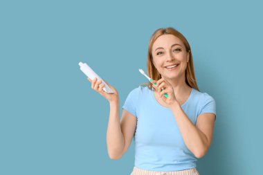 Diş fırçası ve macunu olan güzel olgun bir kadın mavi arka planda bir şey gösteriyor.