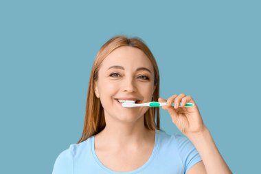 Güzel olgun bir kadın mavi arka planda dişlerini fırçalıyor.