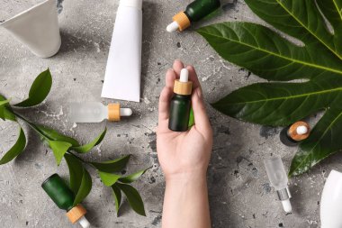 Gri grunge arka planında bir şişe serum olan bir kadın el.