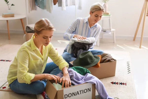Young women putting clothes in boxes for donation at home