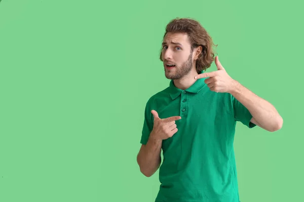 緑の背景に何かを指すTシャツのハンサムな男 — ストック写真