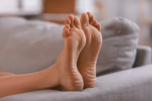 Bare feet of young woman lying on sofa at home, closeup