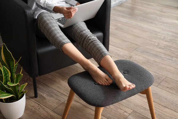 Businesswoman with laptop sitting in armchair at home
