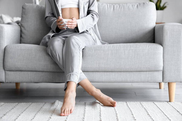 Barefoot woman with cup of tea sitting on sofa at home