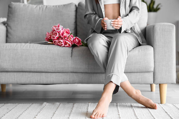 Barefoot woman with cup of tea sitting on sofa at home