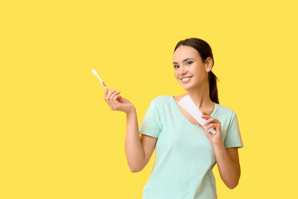 漂亮的年轻女人 有牙膏和黄色背景的刷子 — 图库照片