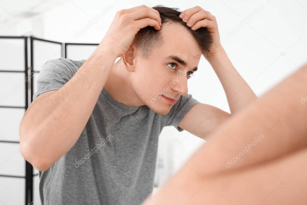 Young brunette man with hair loss problem near mirror in bathroom