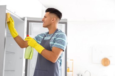 Genç adam mutfakta buzdolabını temizliyor.