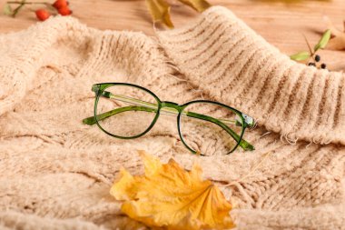Gözlük ve örgü süveter ahşap arka planda, yakın plan.