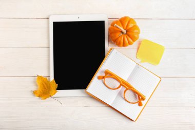 Turuncu gözlüklü kompozisyon, tablet bilgisayar, beyaz ahşap arka planda defter ve balkabağı.
