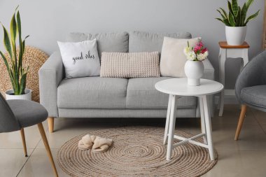 Gri kanepesi, masaları ve çiçekleri vazoda olan modern oturma odasının içinde.