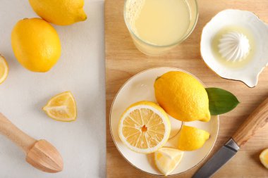 Olgun limonlu ahşap tahta, meyve sıkacağı ve arka planda bir bardak meyve suyu.