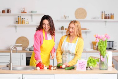 Mutlu genç bir kadın ve annesi evde birlikte yemek pişiriyorlar. Uluslararası Kadınlar Günü kutlamaları