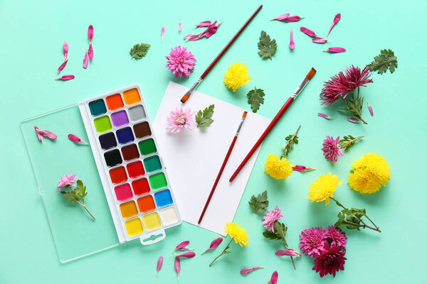 Composition with paints, brushes and chrysanthemum flowers on color background