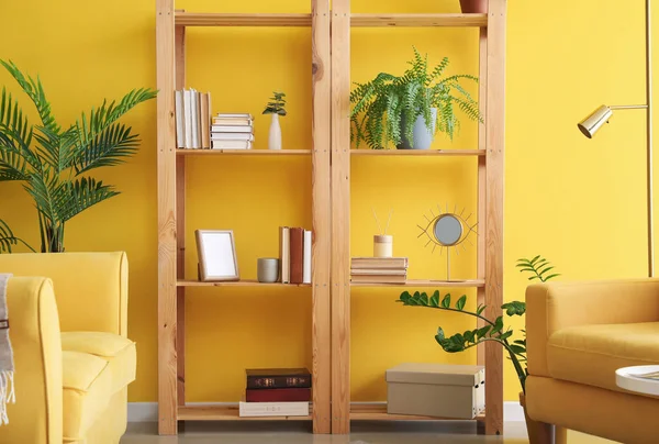 Oturma odasında sarı duvarın yanında dekoru olan ahşap kitaplık.