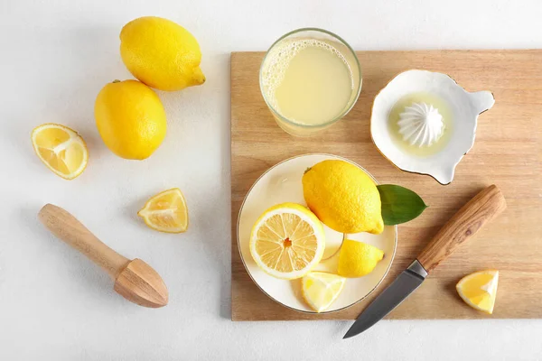 Olgun limonlu ahşap tahta, meyve sıkacağı ve arka planda bir bardak meyve suyu.