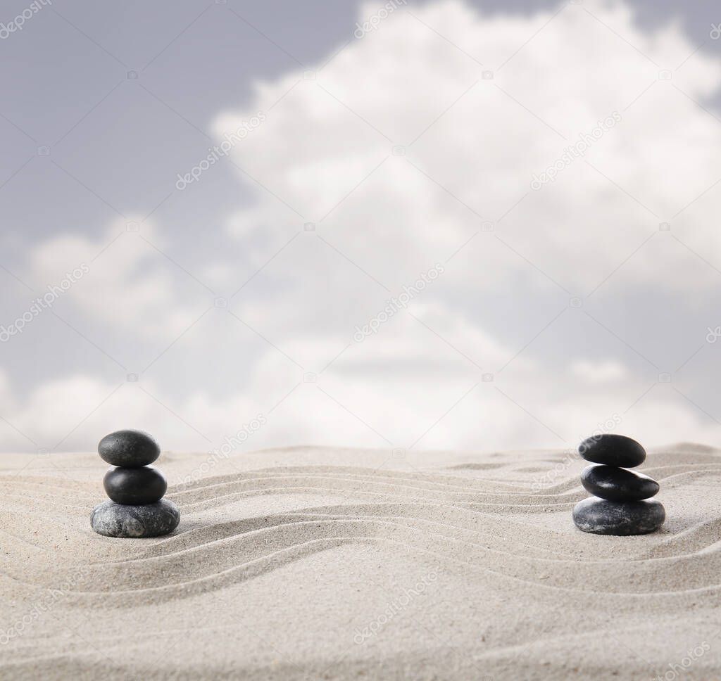 Zen stones on sand with lines against cloudy sky