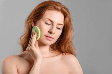 Gri arka planda makyaj süngeri olan güzel bir kadın.