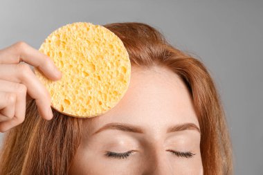 Gri arka planda makyaj süngeri olan güzel kadın, yakın plan.