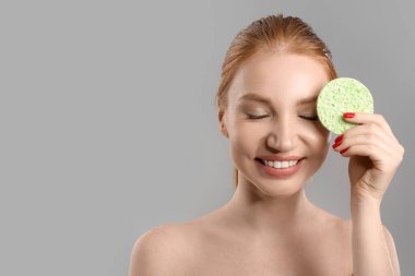 Gri arka planda makyaj süngeri olan mutlu kadın.