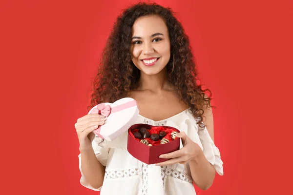 色の背景に箱の中においしいチョコレートキャンディーを持つ美しい若い女性 — ストック写真
