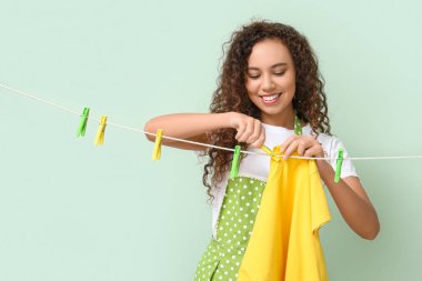 Genç Afro-Amerikalı kadın temiz tişört asıyor. Arka planda mandal var.