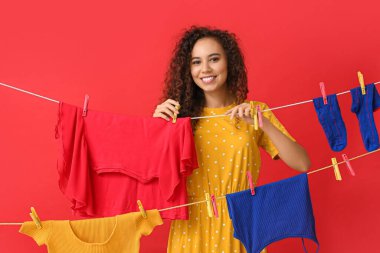 Kırmızı arka planda çamaşır asan ve mandalları olan genç bir Afro-Amerikalı kadın.